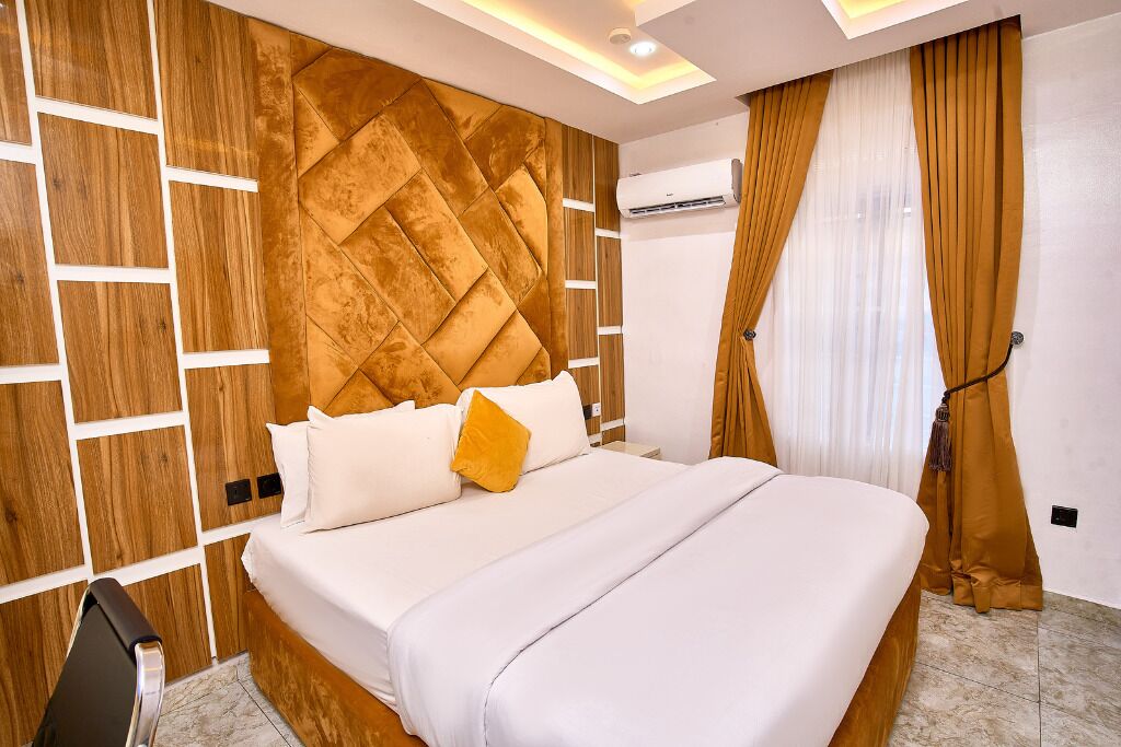 A modern hotel room with a large bed, wooden panel wall, and a ceiling light fixture.