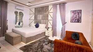 A modern bedroom with a bed, a sofa, a small table, and a decorative mirror. - Libertini Hotel and Apartments (Lekki)