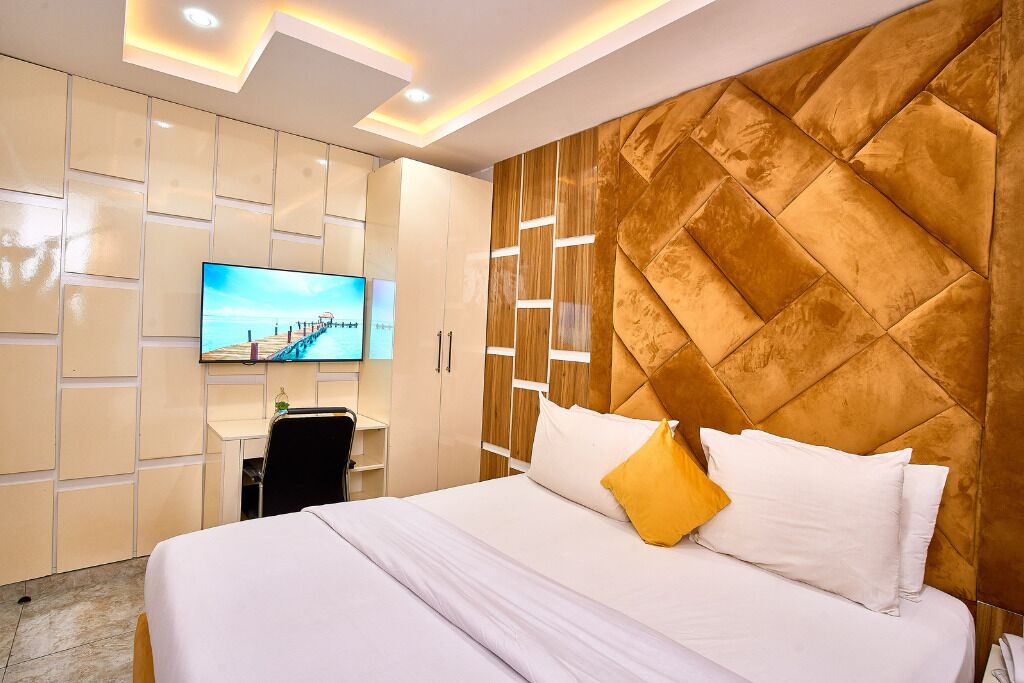A modern hotel room with a large bed, a TV mounted on the wall, and a wooden accent wall.