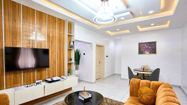 A modern living room with a flat-screen TV, a sofa, a coffee table, and a dining area with a small table and chairs. - Libertini Hotel and Apartments (Lekki)