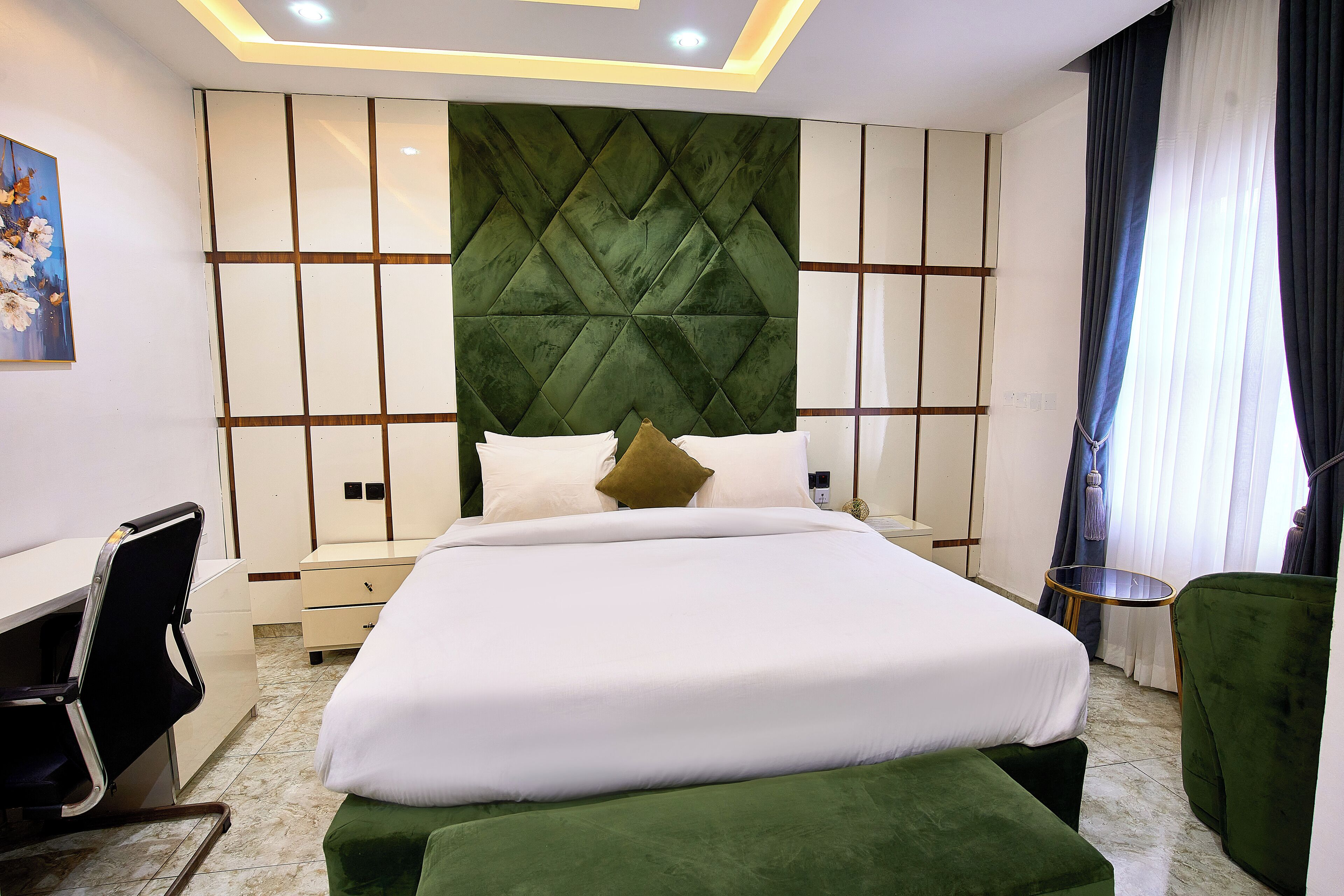 A modern hotel room with a large bed, a desk, and a green ottoman.