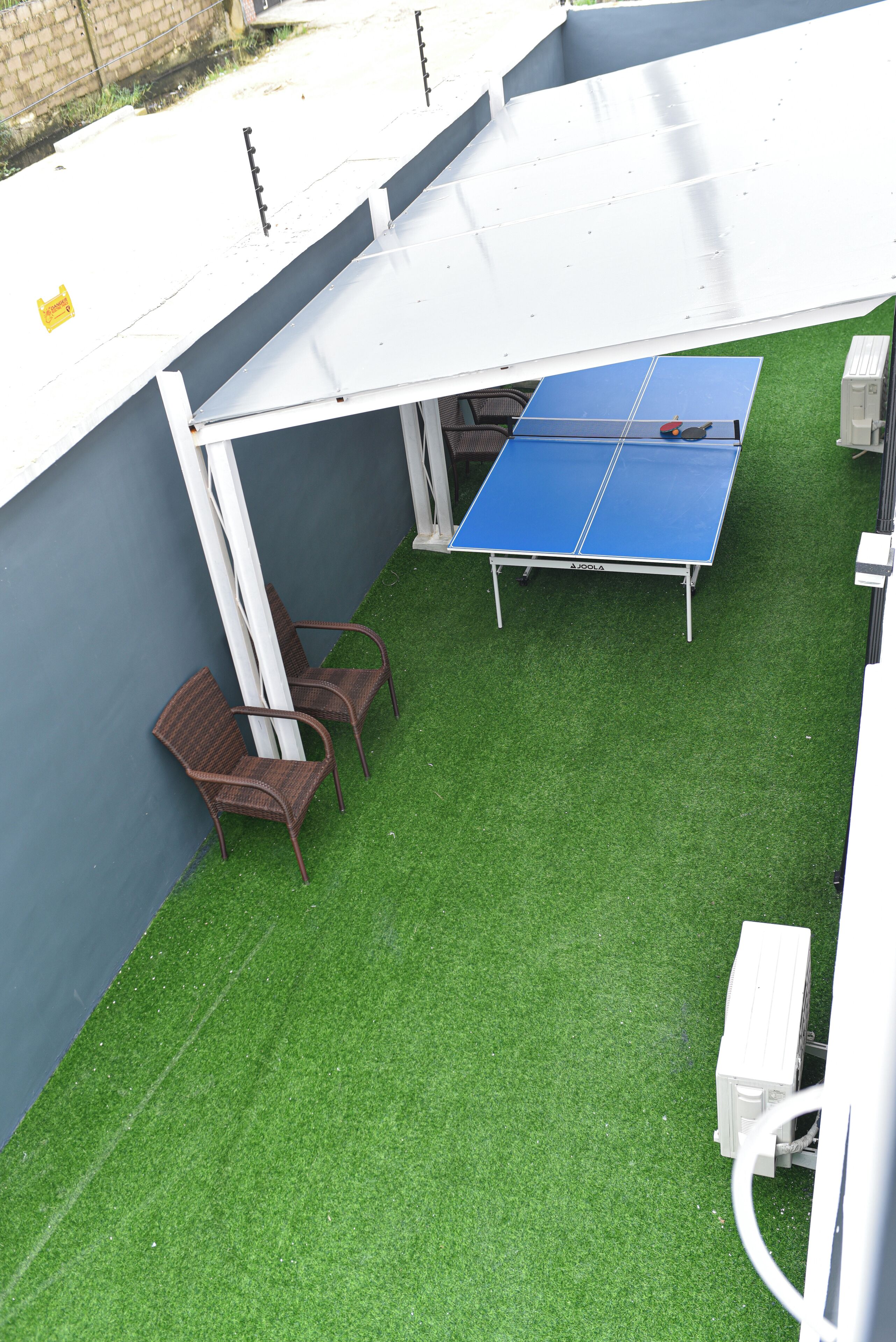 Ein Tischtennis-Tisch mit zwei Stühlen, ein weißes Sonnensegel und künstliches Gras.