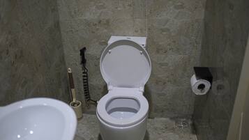 A bathroom with a toilet, a toilet brush, and a toilet paper holder on the wall.