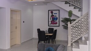 A modern living room with a dining area, a staircase, and a framed artwork on the wall. - Libertini Hotel and Apartments (Lekki)