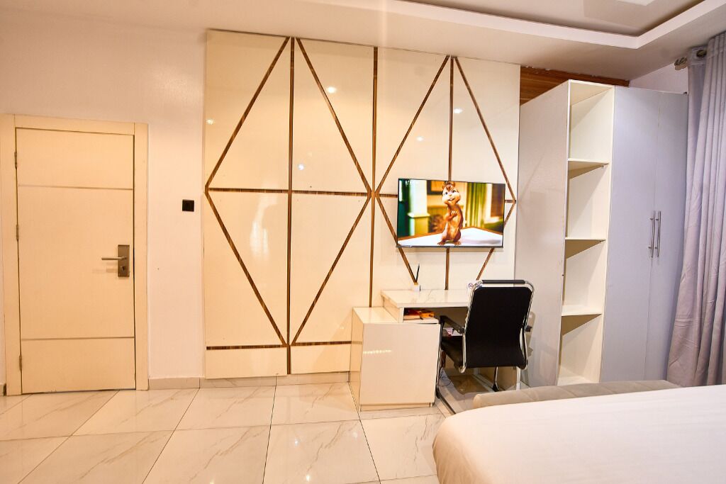 Una habitación de hotel con una cama, un escritorio con silla, un televisor y un armario.