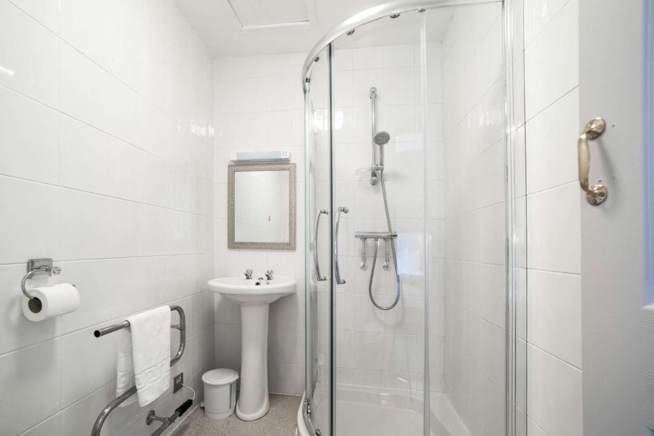 A modern bathroom with a glass-enclosed shower, a pedestal sink, and a toilet.