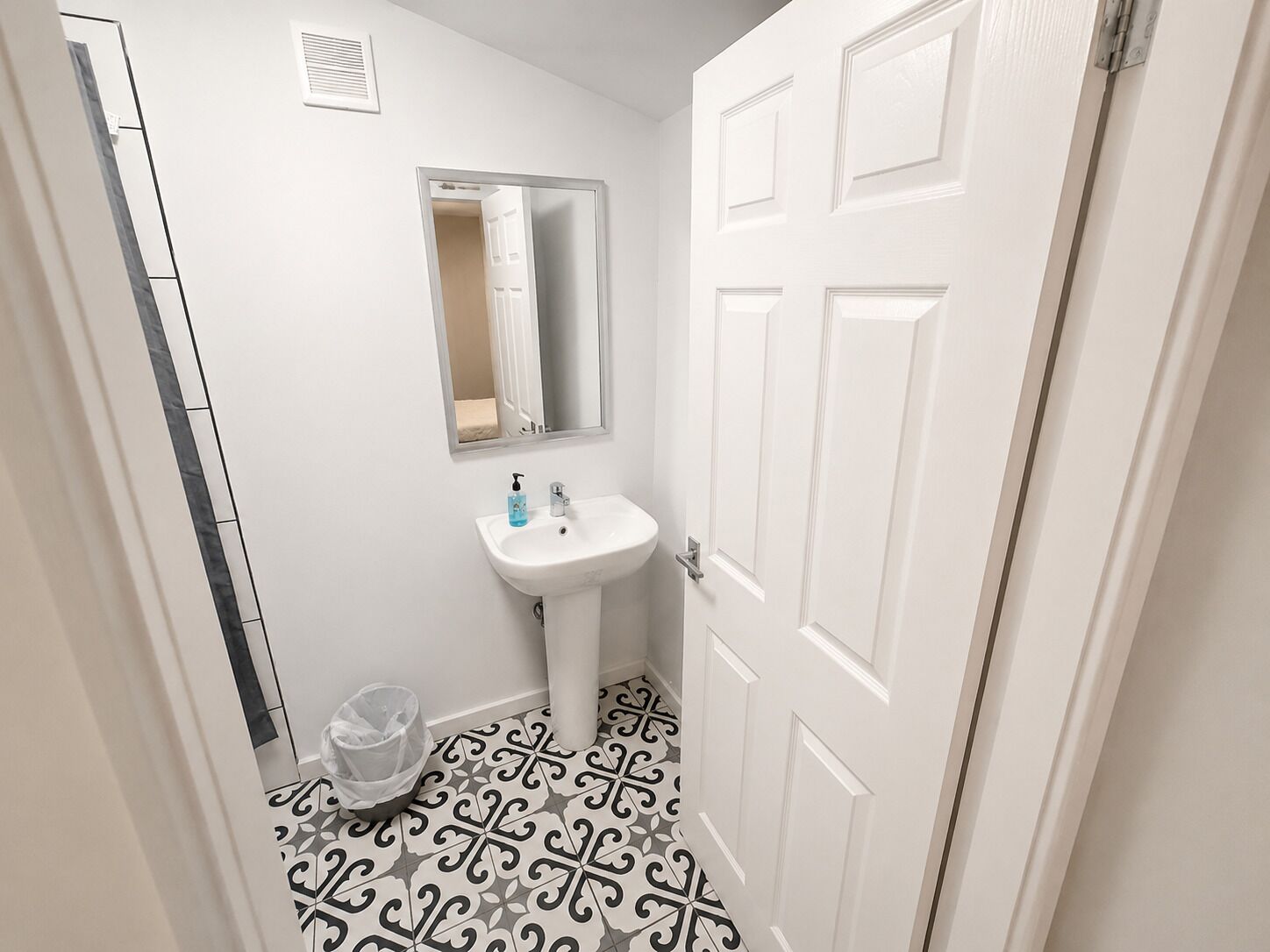 A bathroom with a white sink, a mirror, a patterned floor, and a trash bin.