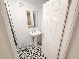 Een badkamer met een witte wastafel, een spiegel, een vloer met een patroon en een prullenbak.