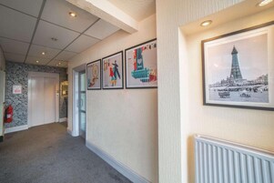 Een gang met ingelijste foto's van bekende bezienswaardigheden, een stenen muur en een brandblusser.