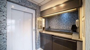A modern kitchen with a stone backsplash, a built-in oven, and a countertop with a phone and a small appliance. - Gresham Hotel Blackpool (Blackpool)