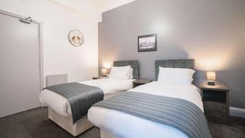 A bedroom with two beds, a white door, a radiator, a framed picture on the wall, and bedside lamps.