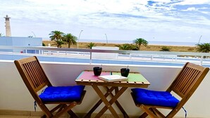 Un balcón con dos sillas de madera y una mesa pequeña, con vista a una playa y un faro.
