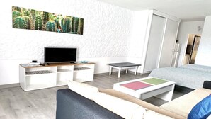 Un dormitorio moderno con una televisión de pantalla plana, una mesita, una cama con cojines coloridos y una gran obra de arte con motivos de cactus en la pared.