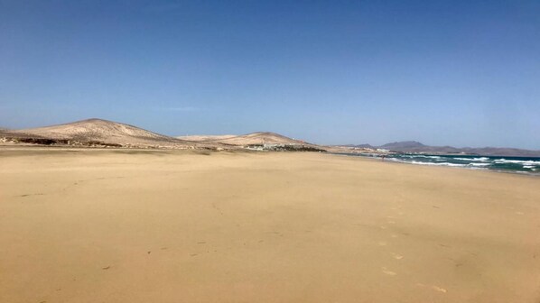 A wide sandy beach with distant hills and a clear sky.