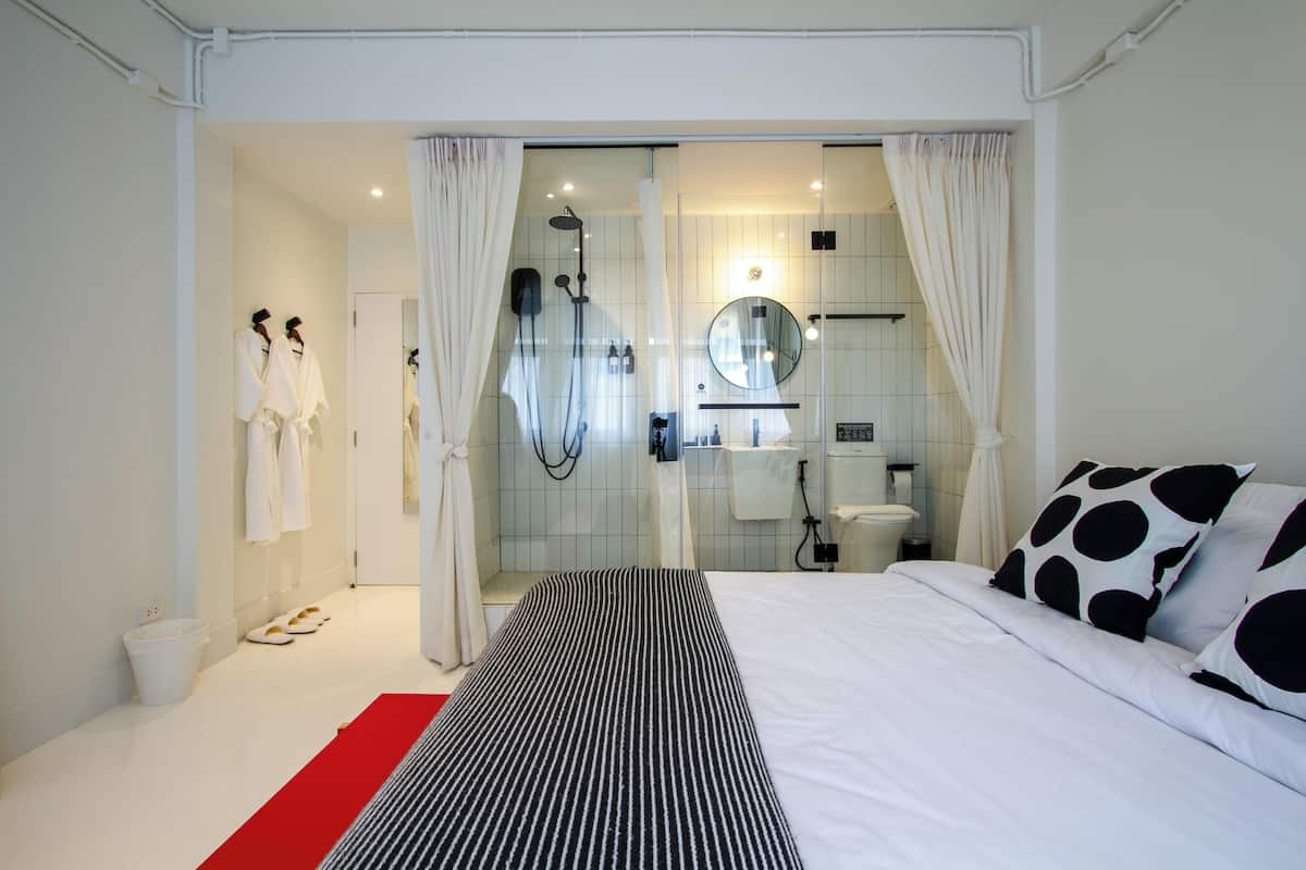 Une chambre d’hôtel moderne dotée d’un grand lit, d’un espace douche et d’une salle de bain avec un miroir et un porte-serviettes.