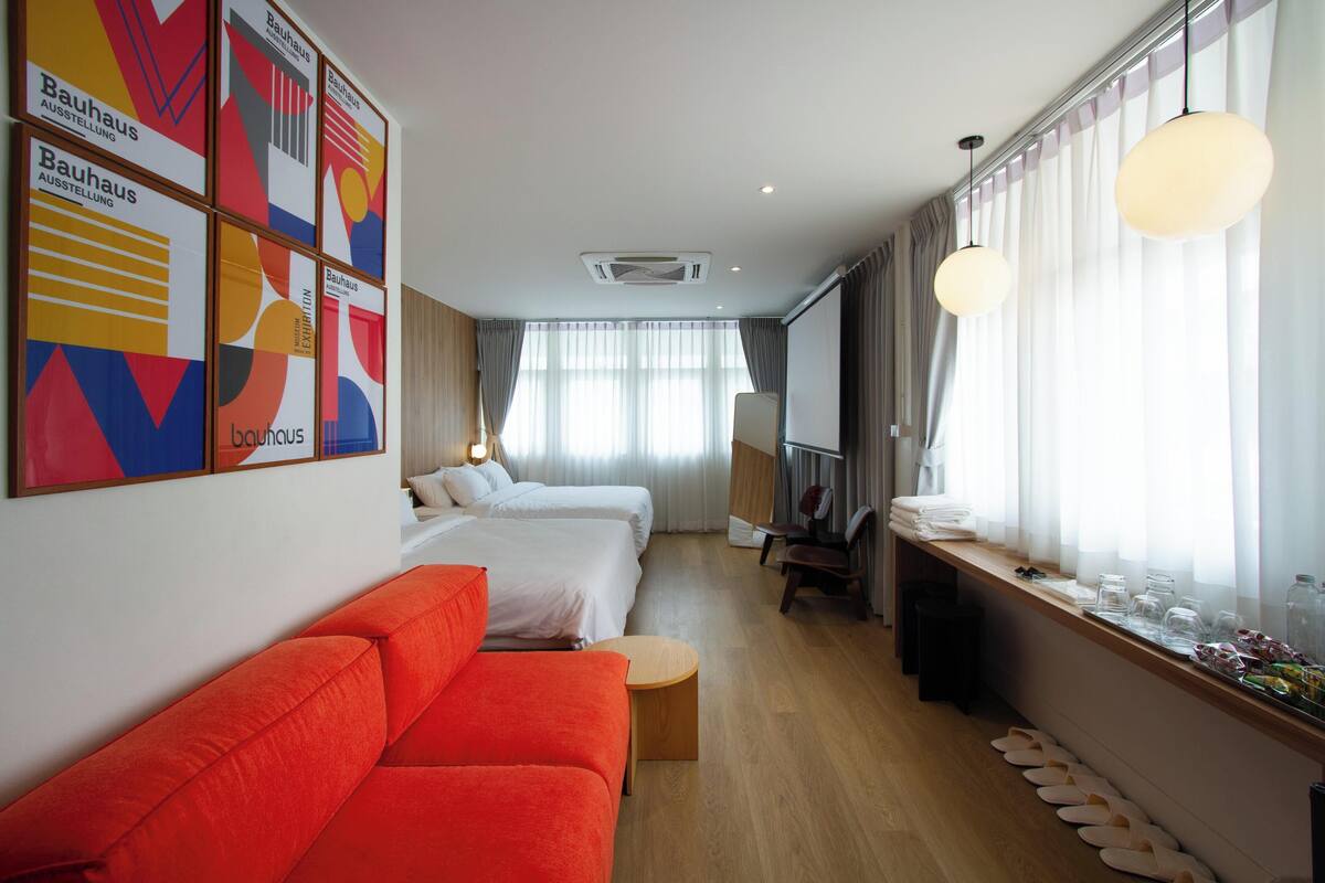 Une chambre d’hôtel avec un canapé, deux lits, une télévision et une fenêtre avec des rideaux.