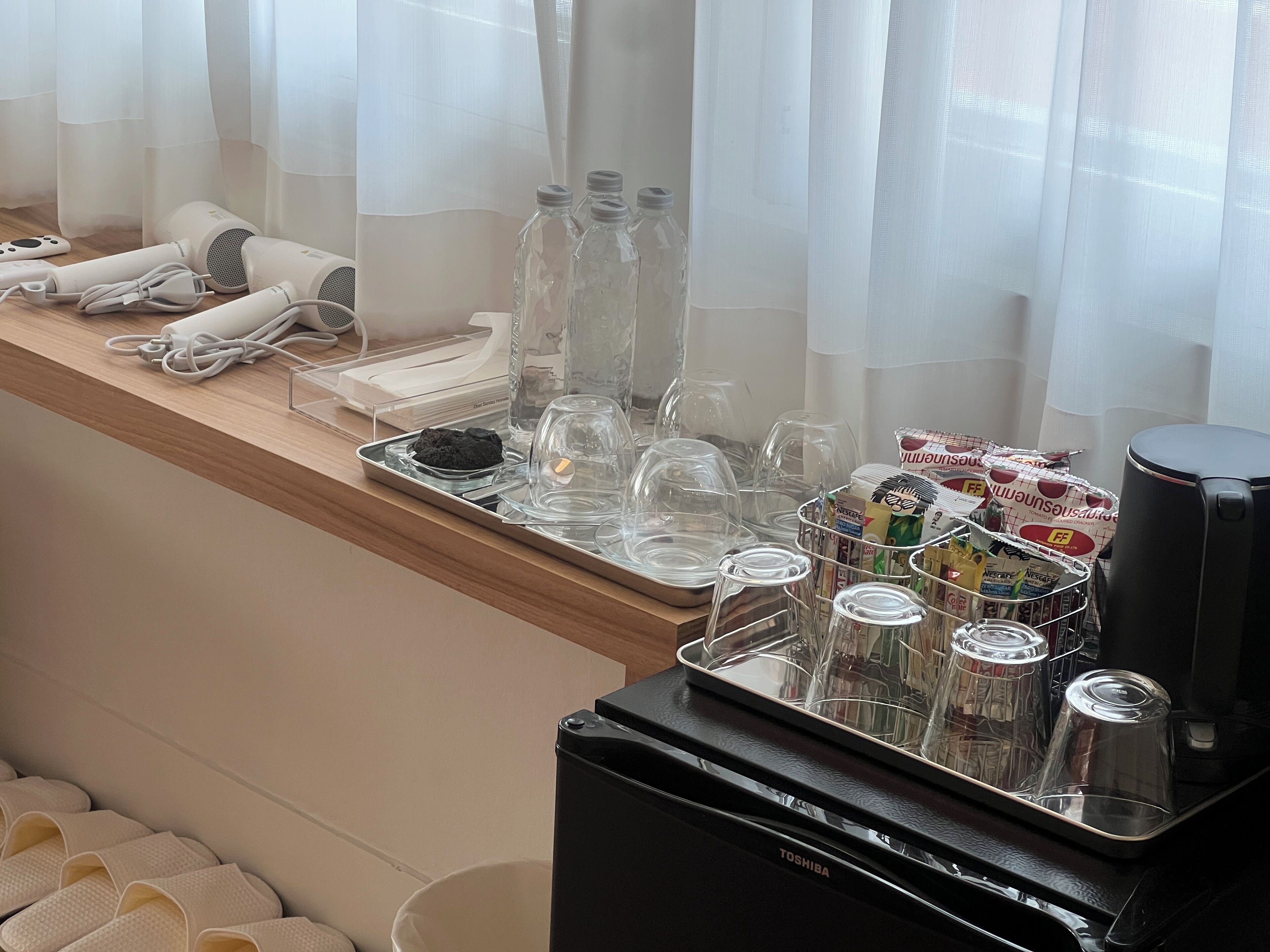 A hotel room with a minibar, a coffee machine, and a tray with glasses, bottles, and a tray with a cookie.