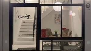 Een winkel voor schoenen met een glazen etalage, een bord waarop 'Zondag' staat en een beveiligingscamera-bord aan de muur.