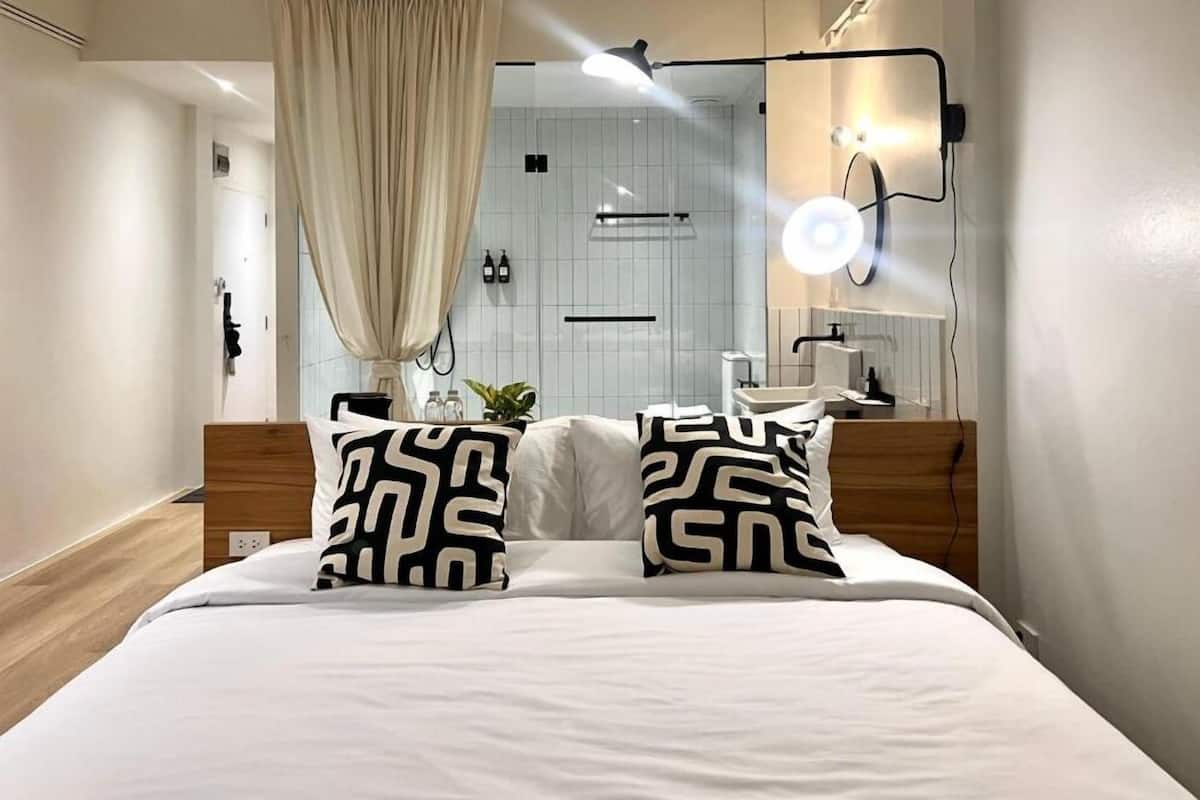 Une chambre d’hôtel moderne équipée d’un lit, d’une table de chevet, d’un miroir et d’un espace douche.