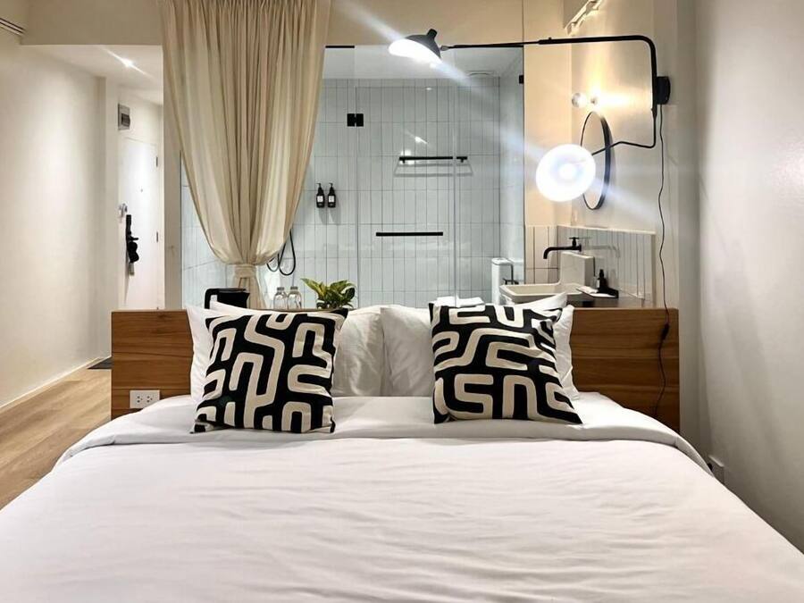 Una habitación de hotel moderna con una cama, una mesita de noche, un espejo y una zona de ducha.