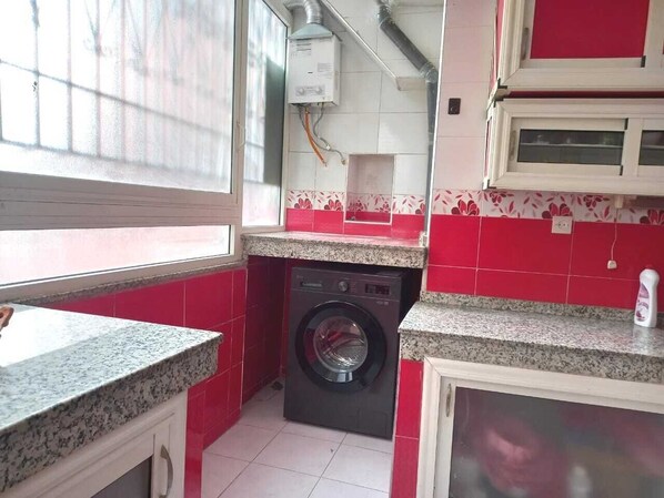 A compact kitchen with a washing machine, red and white tiles, and a window.