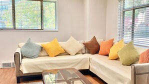 A living room with a sectional sofa, a glass coffee table, and a large window with blinds. - Spacious 3 Bedroom 1 Bathroom  Rogers Park Town House Budget-Friendly (Chicago)