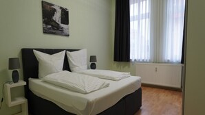 Ein Schlafzimmer mit einem Bett, zwei Nachttischen, einem Wandbild, einem Fenster mit Vorhängen und einer Heizung.
