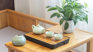 Une table en bois sur laquelle se trouve un plateau avec une théière et des tasses, et une plante en pot à côté.