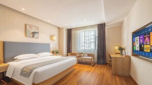 Une chambre d’hôtel avec un grand lit, un bureau, une chaise, une télévision et une fenêtre avec des rideaux.