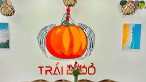 A dining area with a wooden table and chairs, a vase of flowers, and a wall mural featuring a pumpkin with wings and a rooster. - căn hộ biển (Thành phố Phú Quốc)