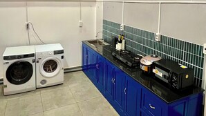 A laundry room with a washing machine, dryer, blue cabinets, a black countertop, and a wooden ceiling with recessed lighting. - căn hộ biển (Thành phố Phú Quốc)