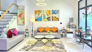 A modern living room with a grey sofa, orange cushions, two round tables, abstract art on the wall, and a staircase with a wooden railing. - căn hộ biển (Thành phố Phú Quốc)