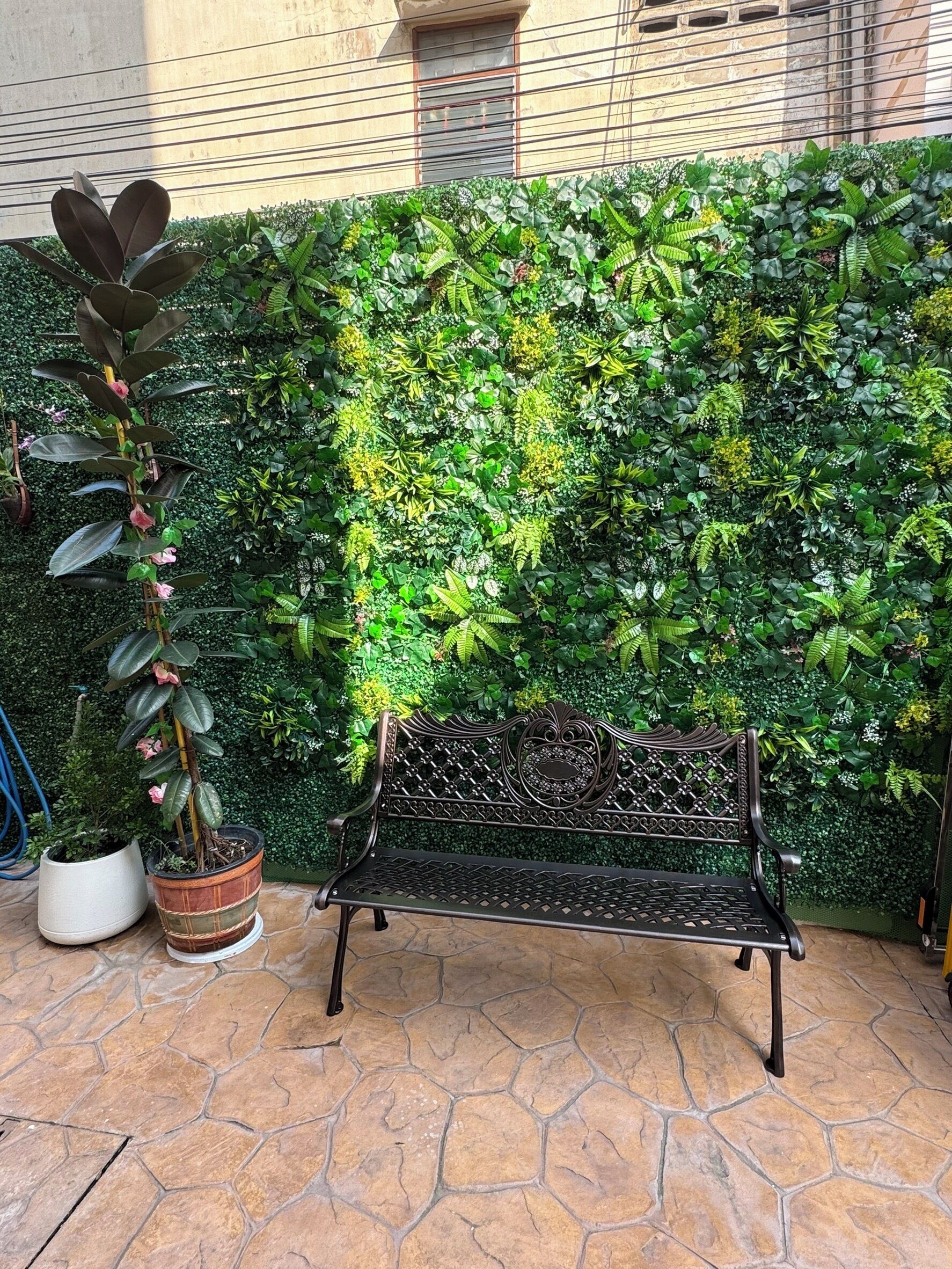A bench with a decorative backrest, positioned in front of a lush green hedge.