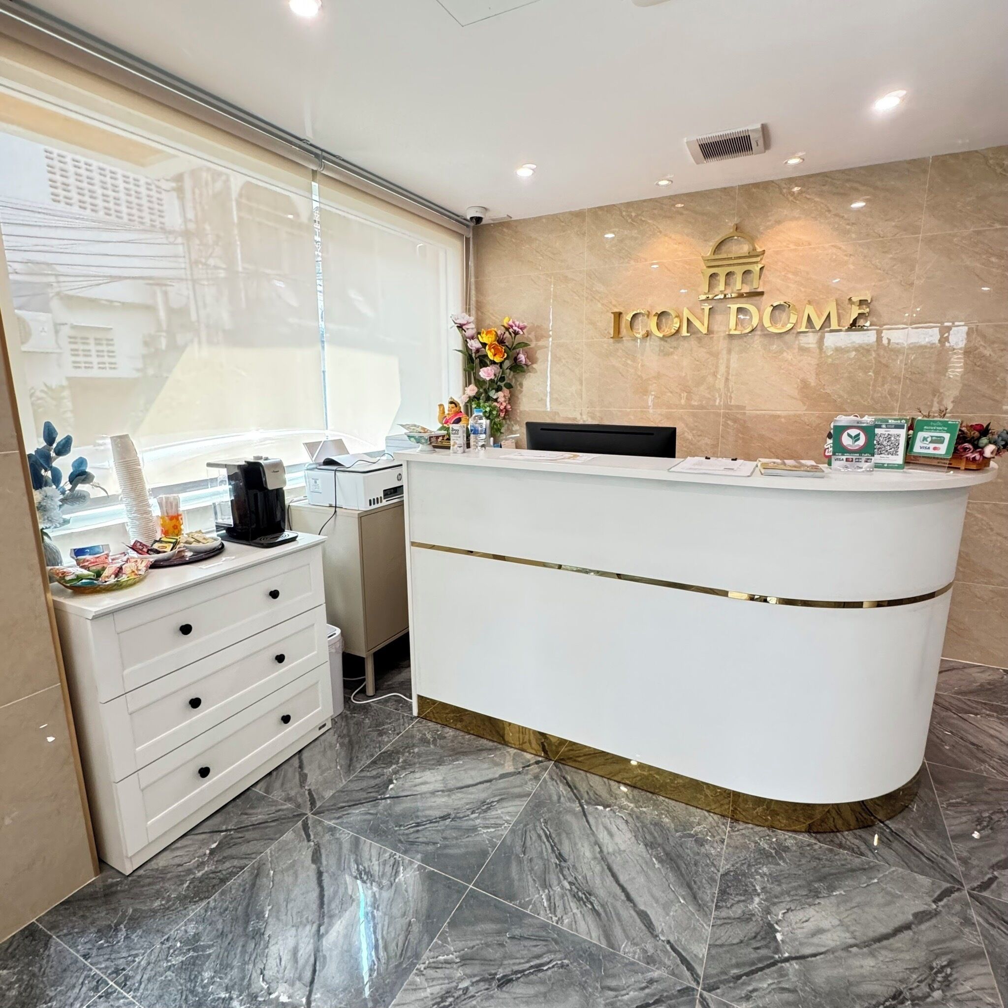 A reception desk with a marble floor, a window with blinds, and a wall-mounted sign that reads "ICON HOME".