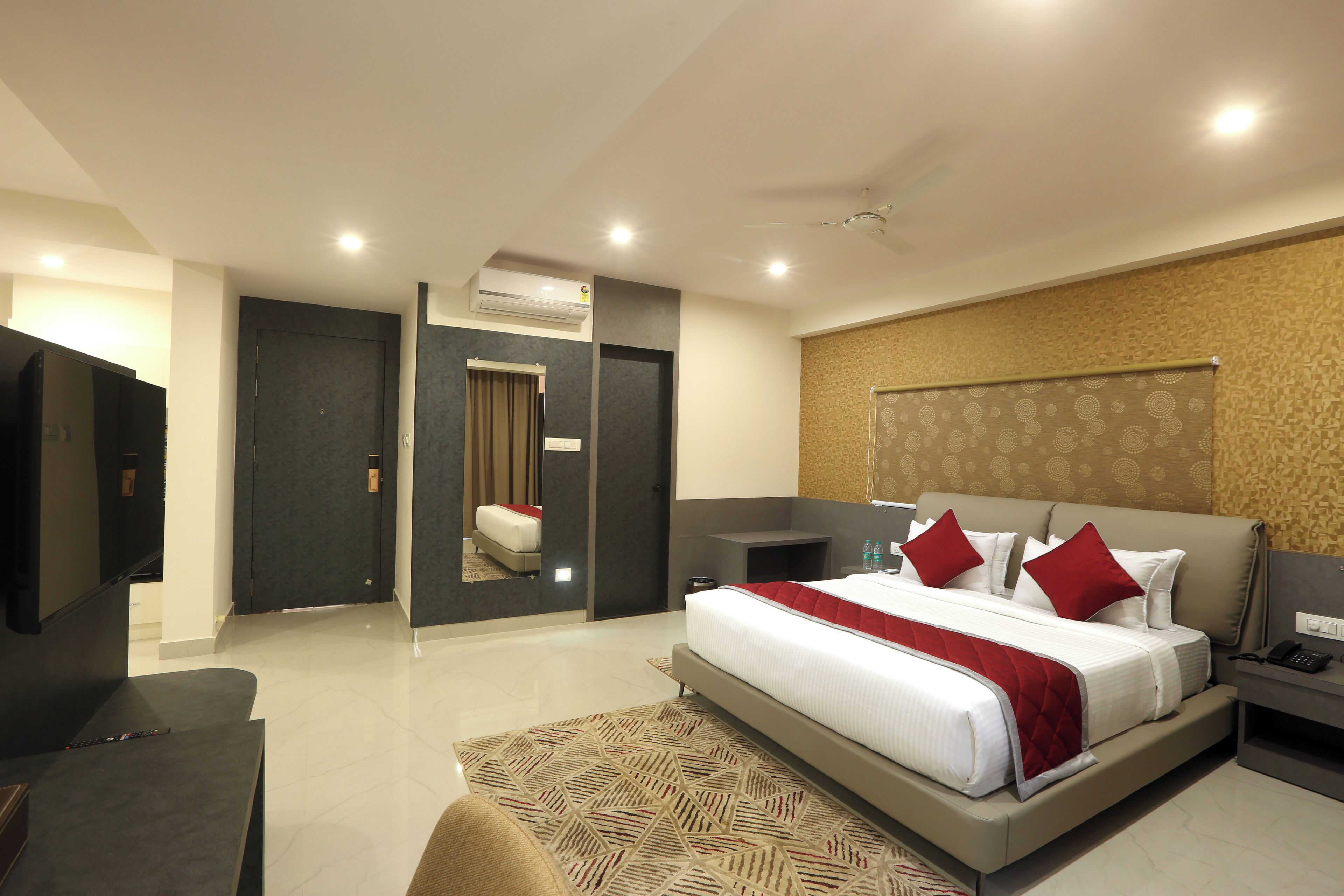 A modern hotel room with a large bed, a bedside table, a TV, and a bathroom visible through an open door.