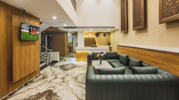 Eine moderne Hotelhalle mit Empfangstresen, einer Sitzecke mit Ledersofas, einem Marmorboden und einem an der Wand befestigten Fernseher.