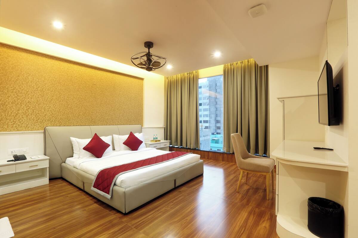 A modern hotel room with a large bed, a desk, a chair, and a TV.