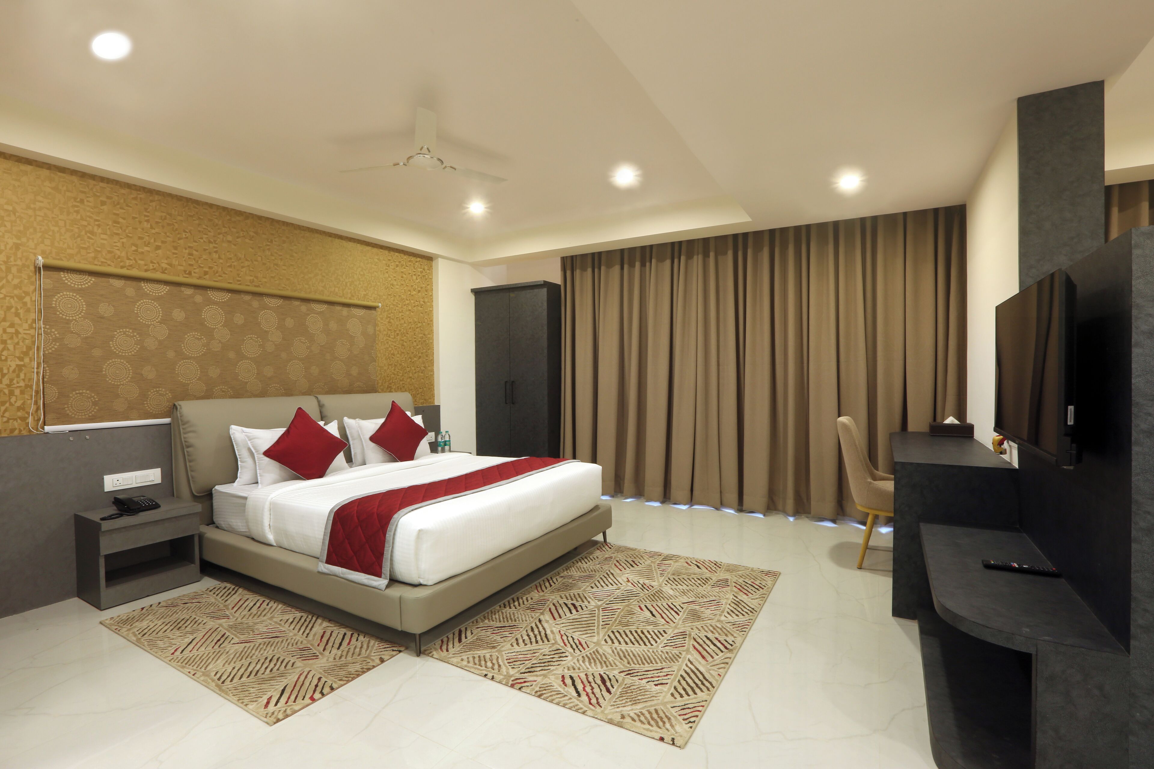 A modern hotel room with a large bed, a desk, a TV, and a ceiling fan.