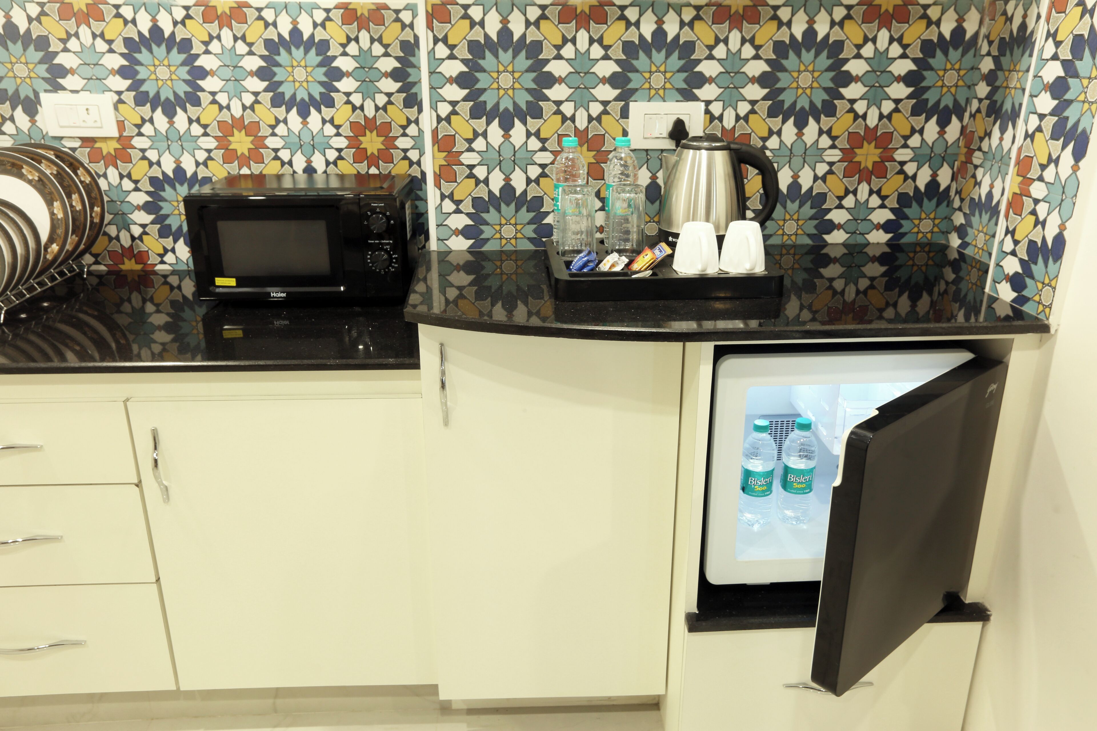 A kitchen with a microwave, a coffee maker, and a refrigerator with water bottles.