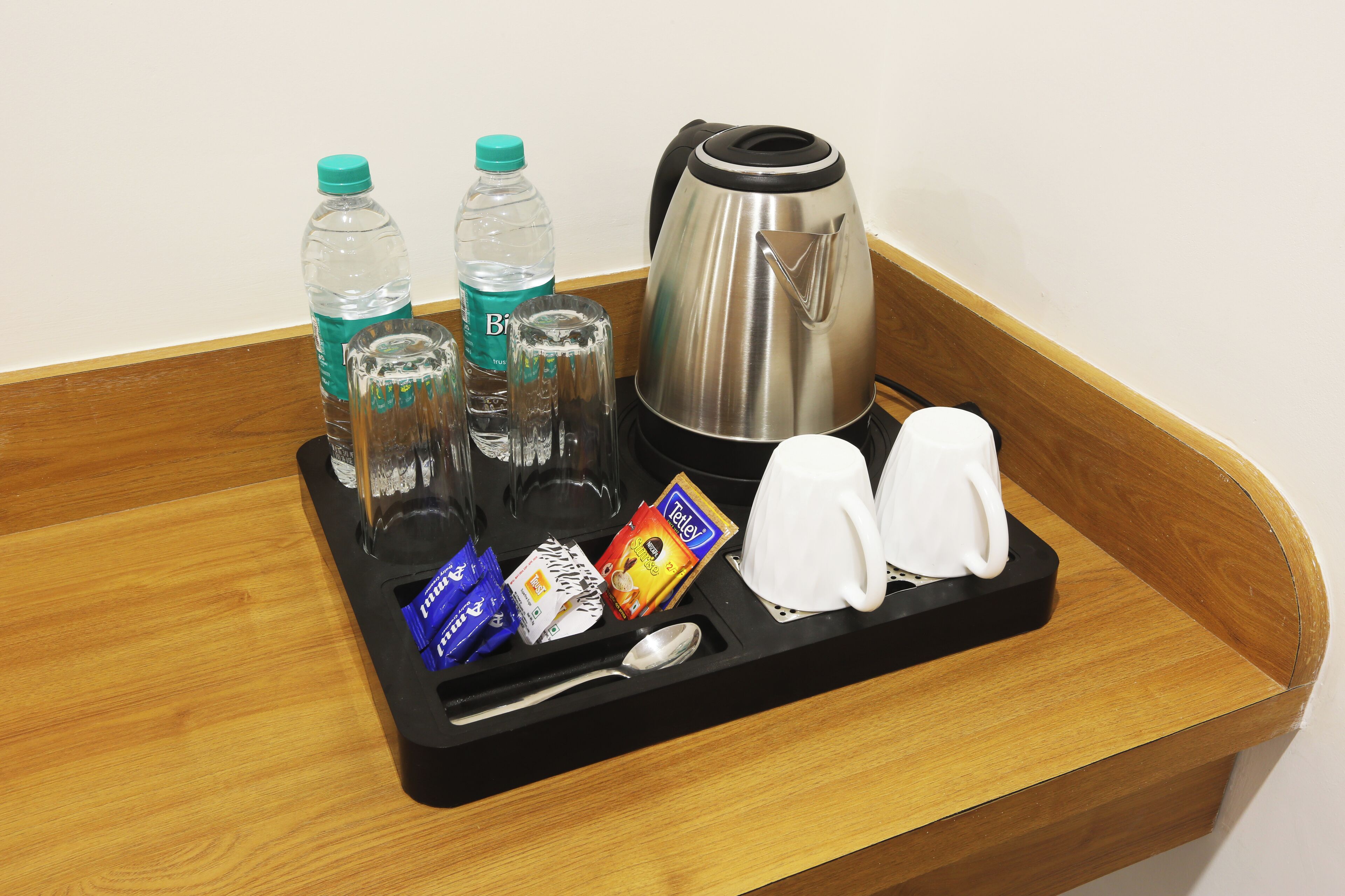 Un vassoio con un bollitore, due bottiglie d'acqua, un bicchiere, una bustina di zucchero, una bustina di panna per il caffè, un cucchiaino e due tazze bianche.