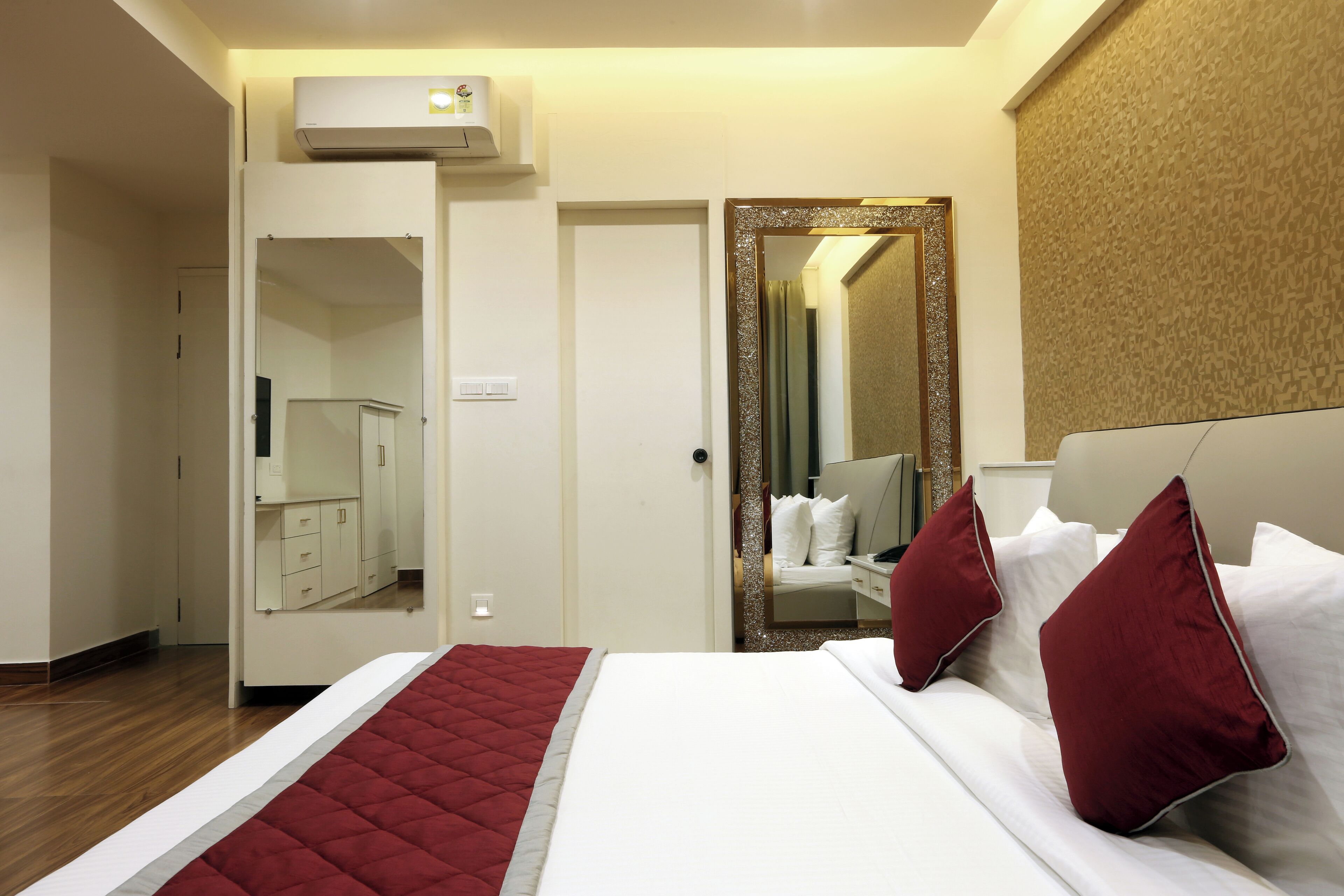 A hotel room with a bed, a wardrobe, a mirror, and an air conditioning unit.