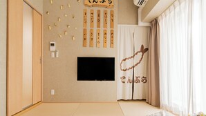 Ett hotellrum med en säng, en tv, en vägg med japansk kalligrafi och ett fönster med gardiner.