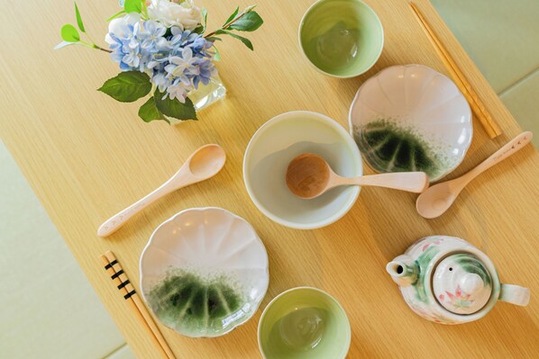 A wooden table with a floral teapot, several bowls, chopsticks, and a vase of flowers. - V Boutique House (Osaka)