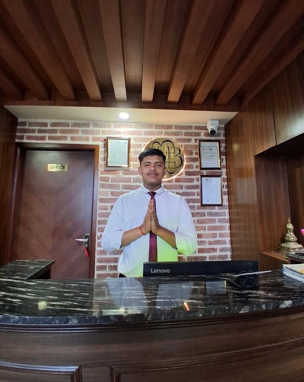 A reception desk with a Lenovo computer, a brick wall, and framed certificates.