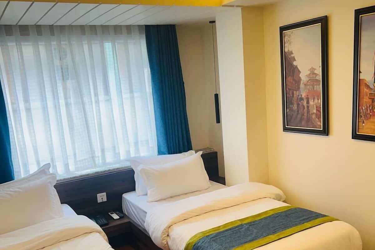 Une chambre d’hôtel avec deux lits, une fenêtre avec des rideaux et deux tableaux encadrés accrochés au mur.