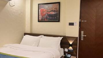 A hotel room with a bed, a nightstand, a wall-mounted air conditioner, a door, and a framed artwork on the wall.