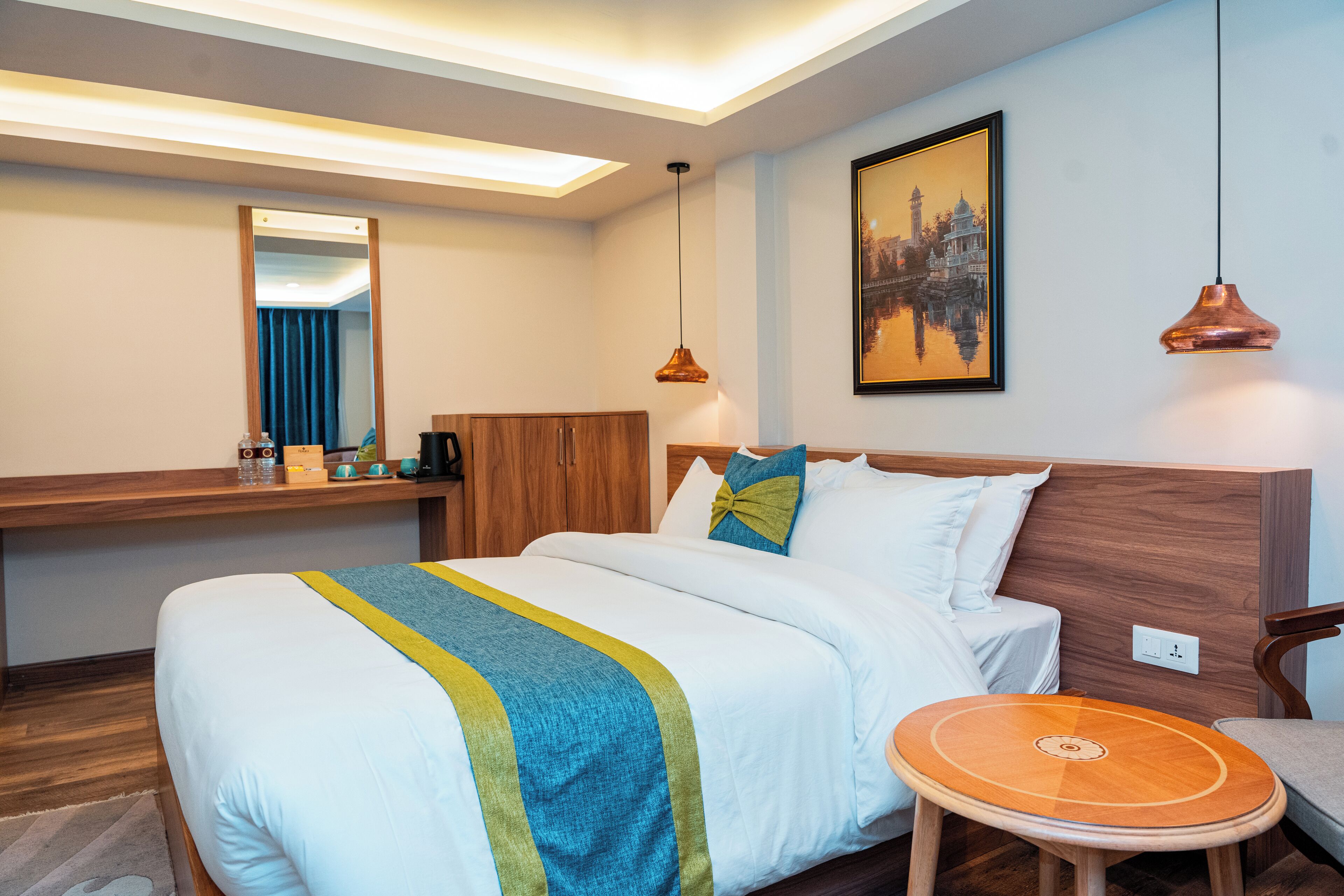 A hotel room with a large bed, a wooden headboard, a bedside table with a lamp, and a small round table.