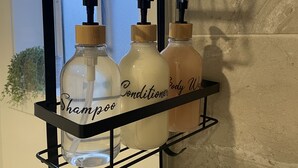 A bathroom shelf holding three bottles of shampoo, conditioner, and body wash. - Cosy Private Studio (West Bathurst)