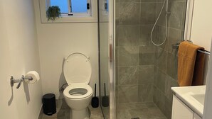 A bathroom with a toilet, a shower with a glass door, a window above the toilet, and a towel rack with a towel. - Cosy Private Studio (West Bathurst)