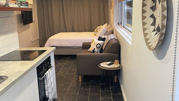 A compact hotel room with a kitchenette, a bed, a sofa, and a dining area. - Cosy Private Studio (West Bathurst)